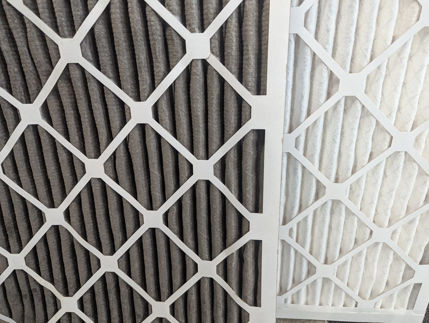 A dirty grey pleated AC filter next to a clean white pleated AC filter of the same type